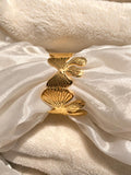 A gold-toned metal cuff bracelet with three textured, fan-like leaf or ginkgo-inspired segments, displayed on draped white satin fabric over a soft cream fleece background.