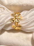 A close-up of a gold flower-shaped hair accessory or hair clip styled with draped white satin ribbon on a soft cream fabric background.