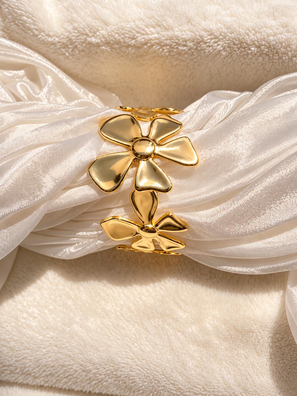 A close-up of a gold flower-shaped hair accessory or hair clip styled with draped white satin ribbon on a soft cream fabric background.