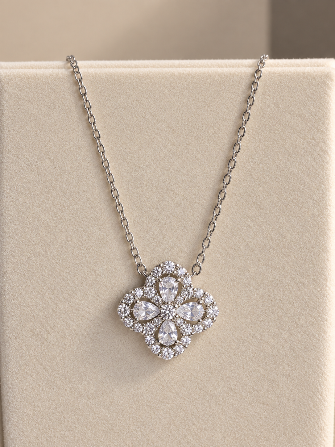 A silver-tone floral pendant necklace with clear stones, displayed on a beige jewelry bust.