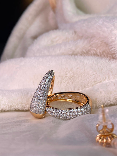 A gold ring with pavé-set clear stones, displayed on a soft white textured fabric background.