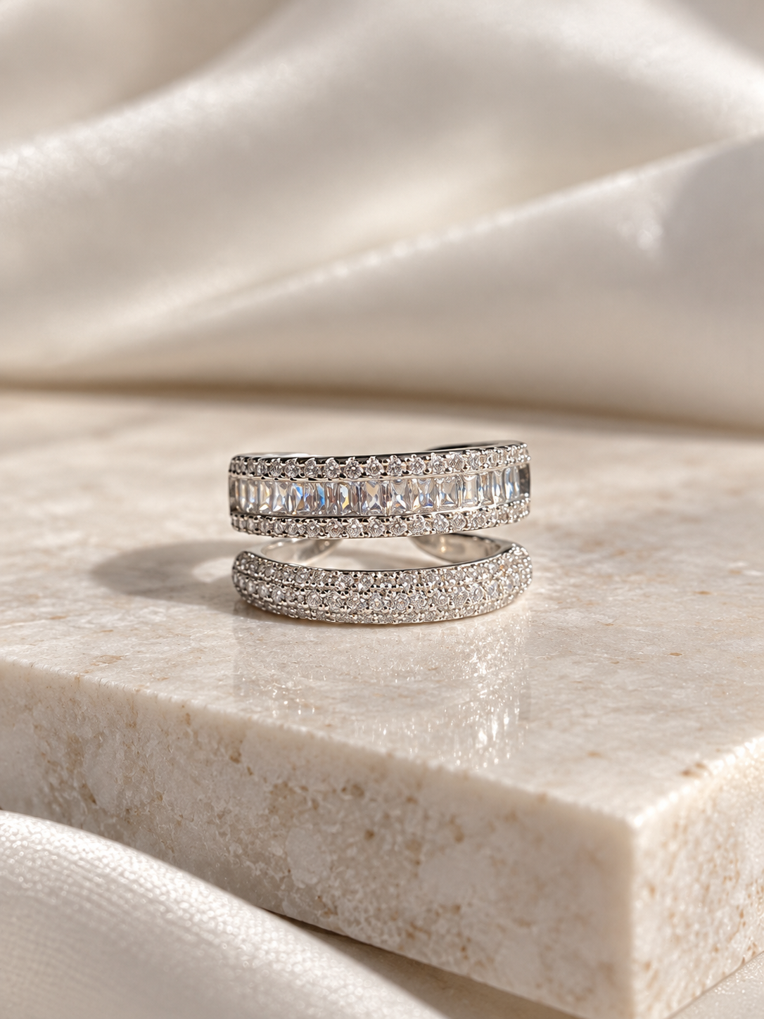 Adjustable silver-tone ring featuring a wide band of sparkling clear baguette-cut crystals with smaller round crystal accents, displayed on a cream marble surface.