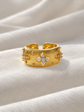 Adjustable gold-tone statement ring featuring textured floral motifs with sparkling clear crystals, displayed on soft white fabric.