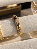 Gold-tone statement ring featuring a textured band with sparkling clear crystal accents, displayed on a cream marble surface.