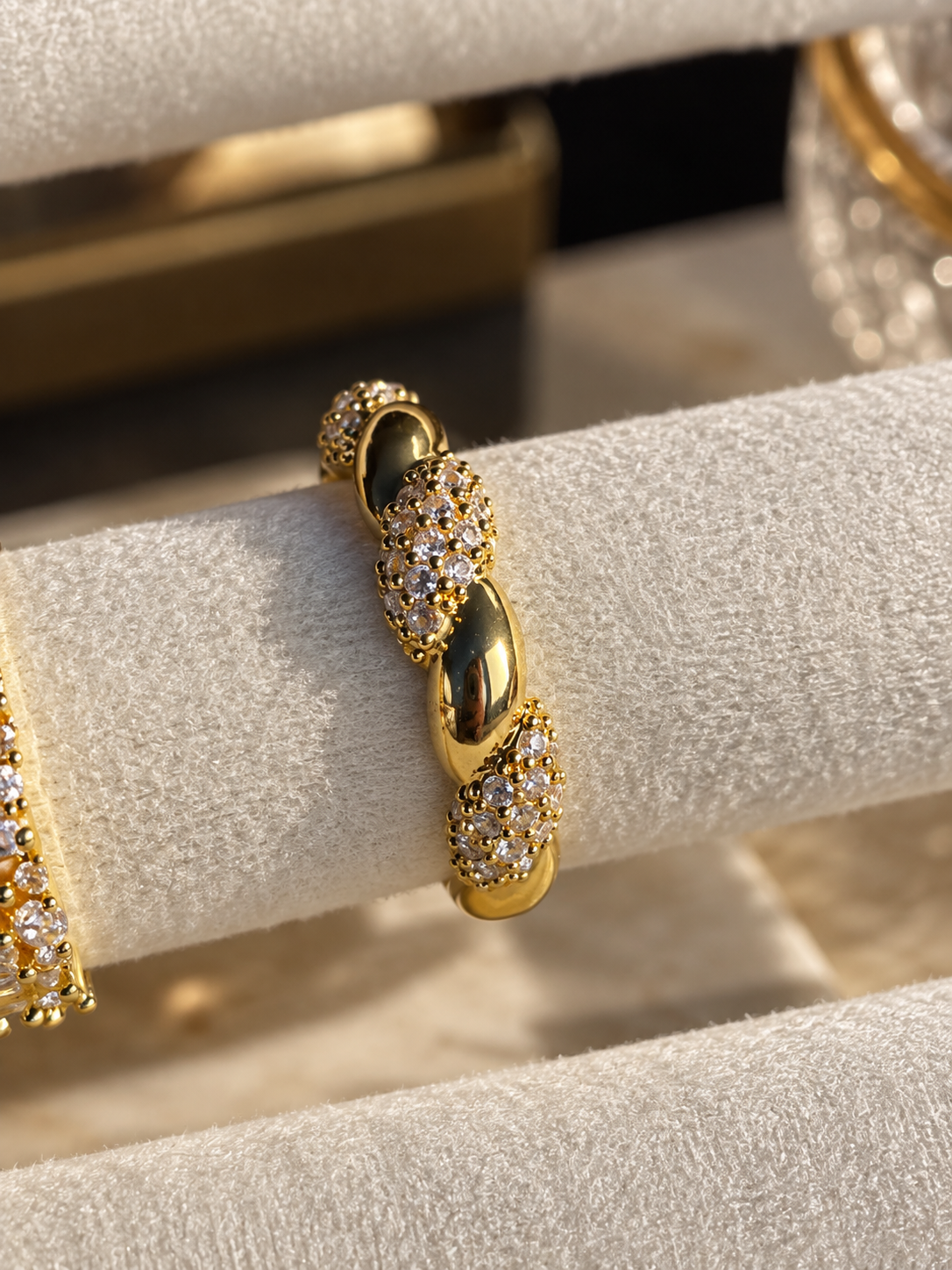 Gold-tone statement ring featuring a textured band with sparkling clear crystal accents, displayed on a cream marble surface.