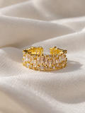 Adjustable gold-tone ring featuring rows of sparkling clear baguette-cut crystals and smaller round crystals, displayed on soft cream fabric.