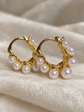 Gold-tone hoop earrings decorated with smooth white faux pearls around the lower half, displayed on soft cream fabric.