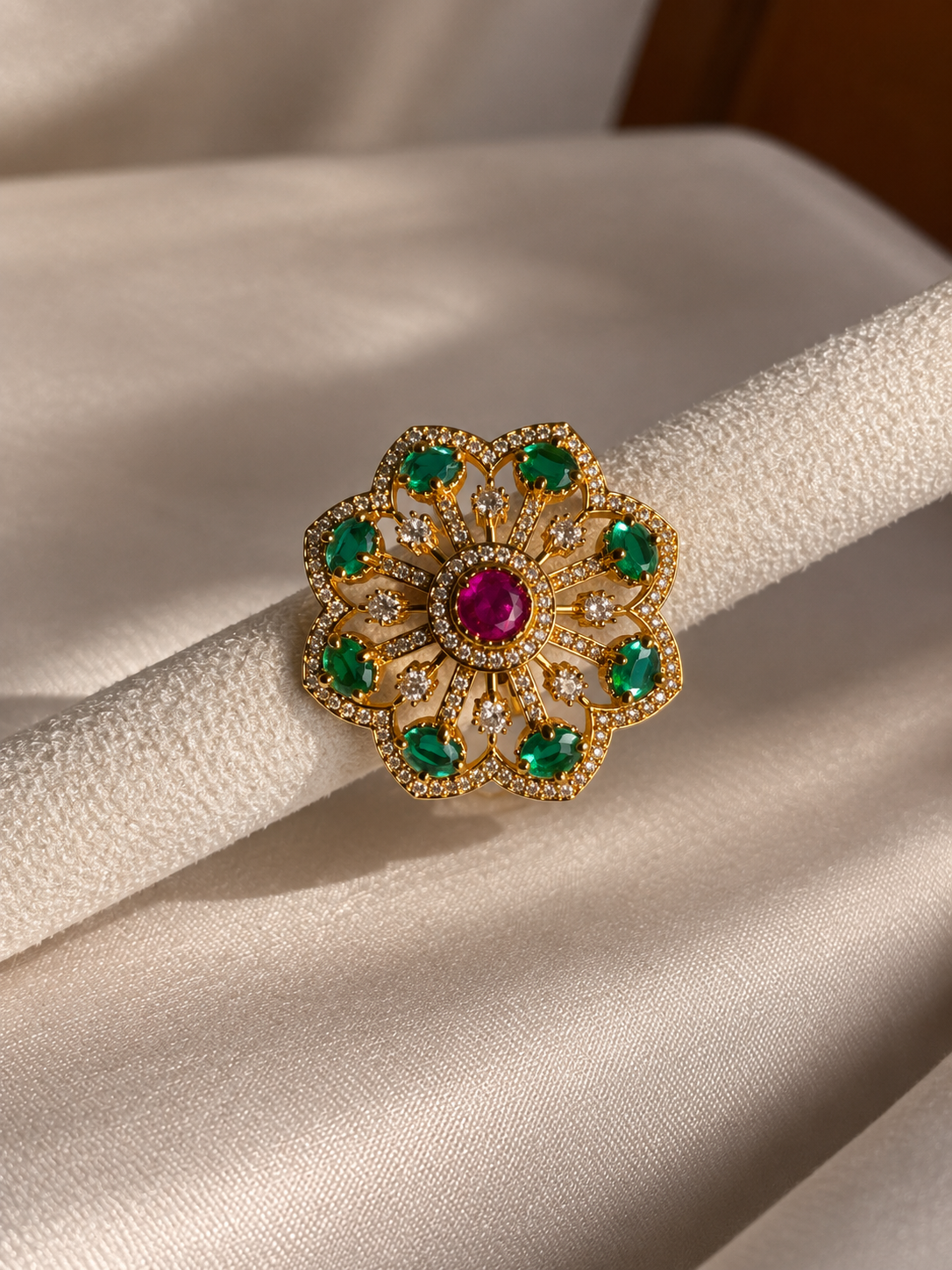 Gold-tone floral statement ring featuring vibrant emerald-green stones, a deep ruby-red center stone, and sparkling clear crystal accents.