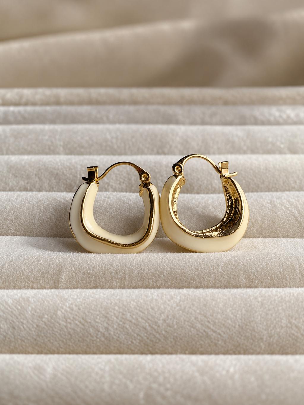 Ivory hoop earrings with polished gold-tone edging, featuring a smooth curved design displayed on soft cream fabric.