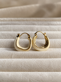Ivory hoop earrings with polished gold-tone edging, featuring a smooth curved design displayed on soft cream fabric.