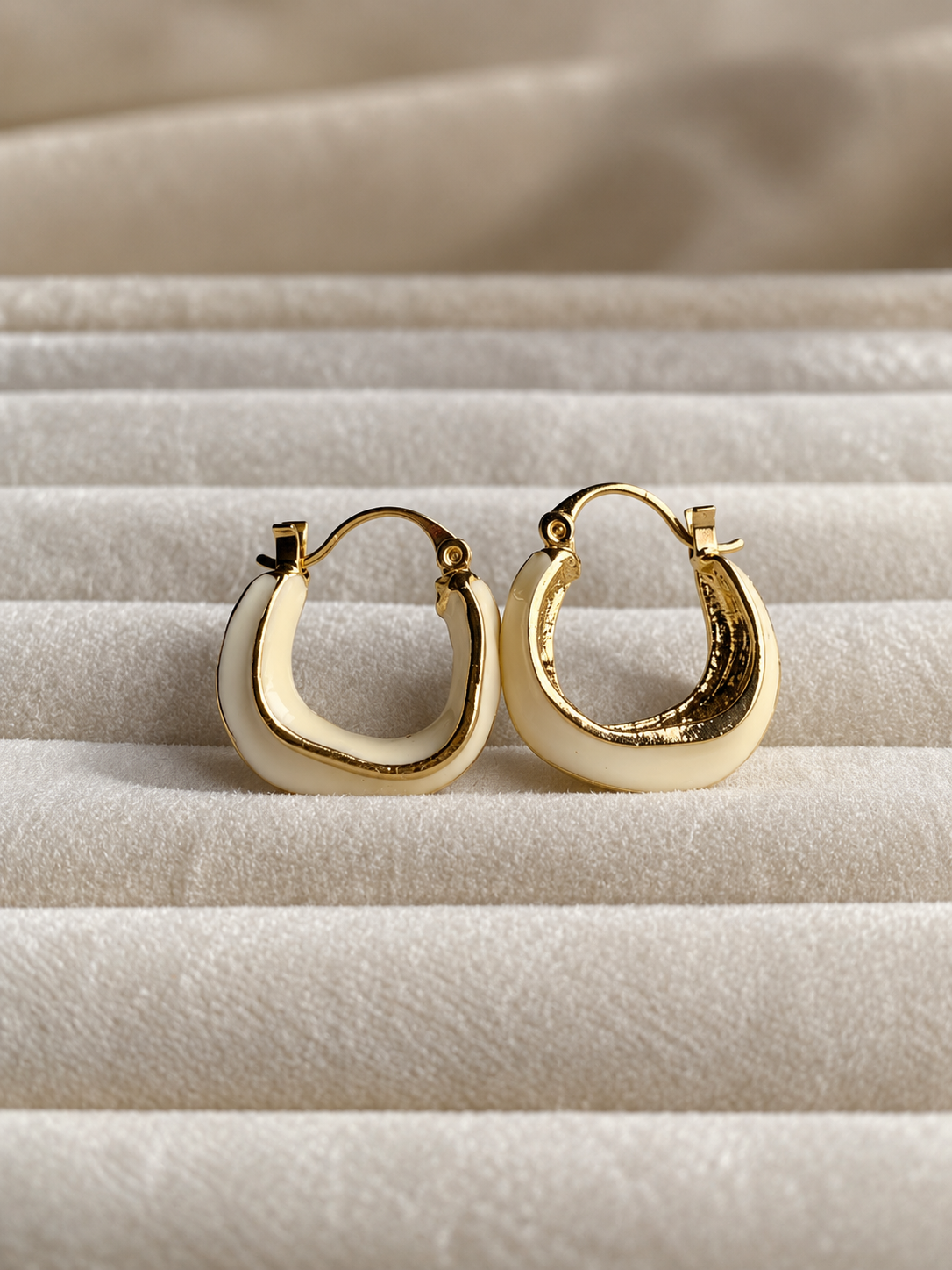 Ivory hoop earrings with polished gold-tone edging, featuring a smooth curved design displayed on soft cream fabric.