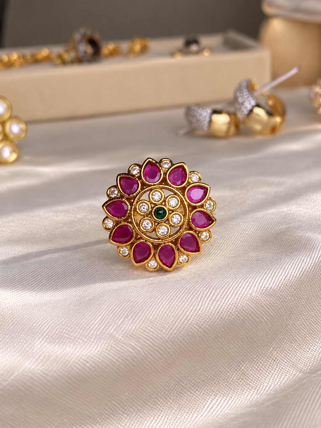 South Indian Kundan-style statement ring with a gold-tone floral mandala design, deep ruby-red petal stones, clear accents, and a small emerald-green center stone.