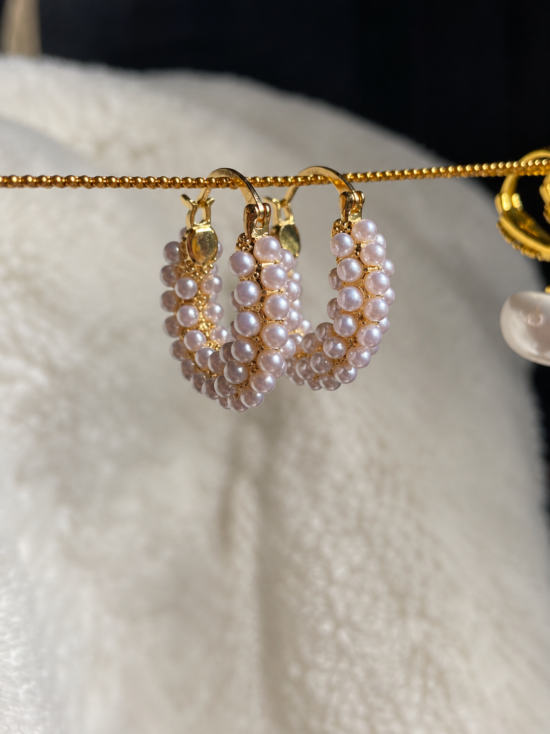 Gold-tone hoop earrings adorned with clusters of small blush pink and white pearls, displayed against soft cream fabric.