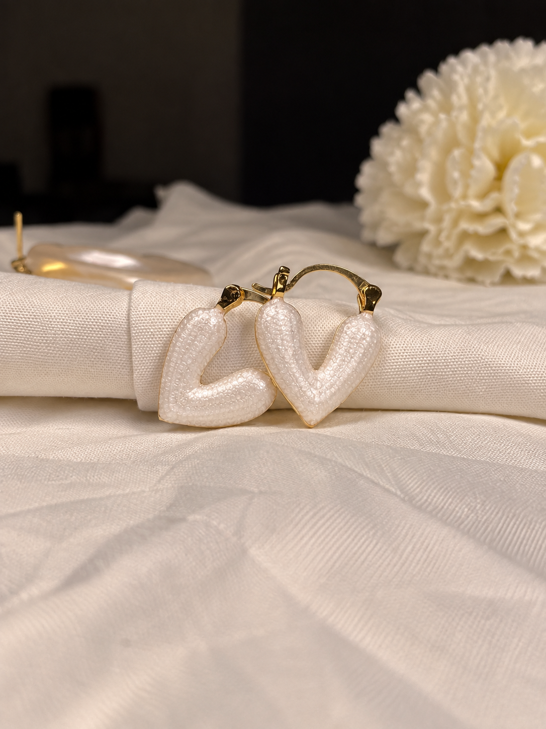 White textured heart-shaped hoop earrings with polished gold-tone edges, featuring an open-heart curved design on cream fabric.